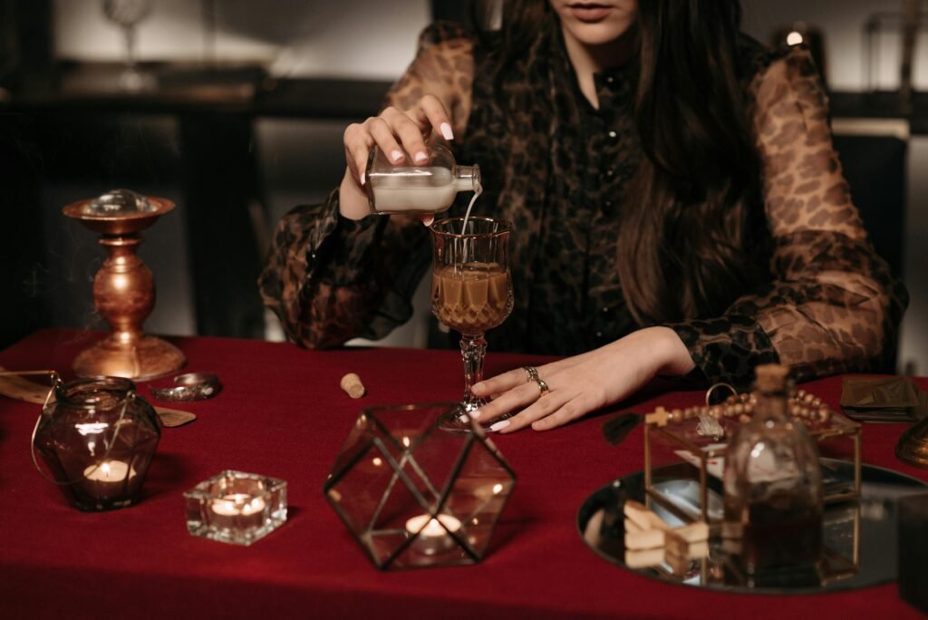 A woman pours a mysterious liquid into a glass, surrounded by candles and mystical objects.